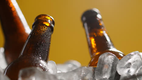 Close-Up-Of-Glass-Bottles-Of-Cold-Beer-Or-Soft-Drinks-Chilling-In-Ice-Filled-Bucket-Against-Yellow-Background